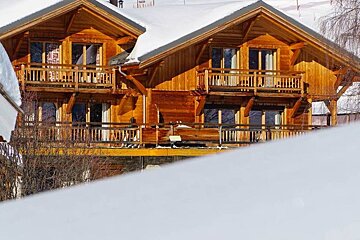 A wooden house with a balcony is covered in snow