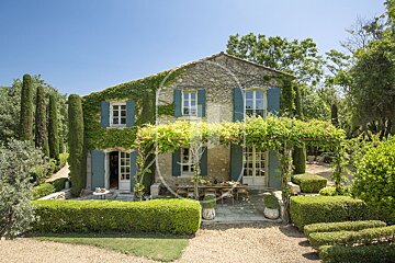 A house with blue shutters is surrounded by trees and bushes