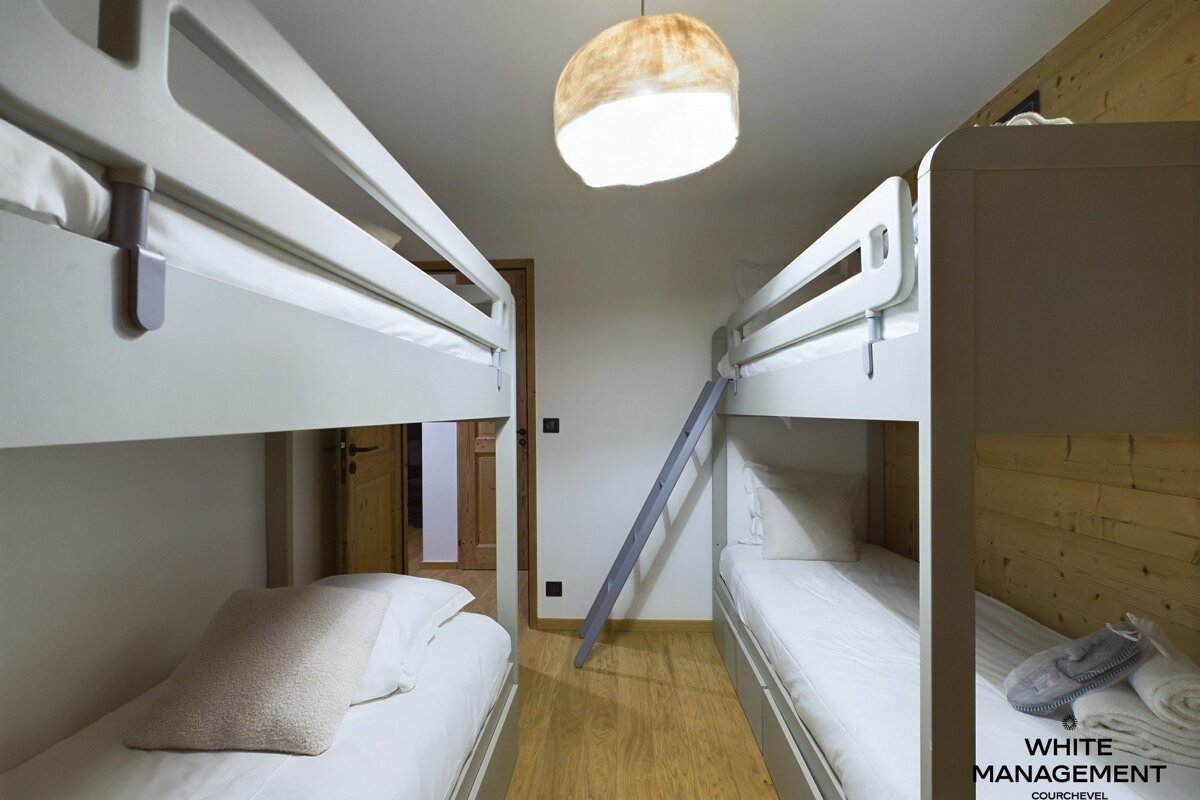 A modern room with two grey bunk beds, a light wood floor, and a unique hanging lamp, offering cozy accommodation.