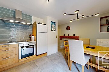 A bright, open-plan kitchen and dining area. Features light wood cabinets, blue tiled backsplash, stainless steel appliances, and a wooden dining table.