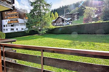 A balcony overlooking a lush green field with a few buildings in the background