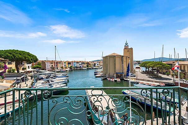 A vibrant view of Port Grimaud, France, featuring colorful houses along its canals filled with boats, a prominent clock tower, and a bright blue sky.