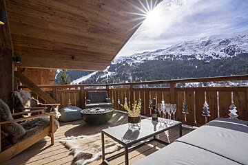 A bottle of champagne sits on a table on a balcony overlooking snow covered mountains