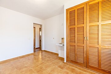 Empty room with white walls, terracotta tile flooring, a small sink, and a large wooden louvered closet.
