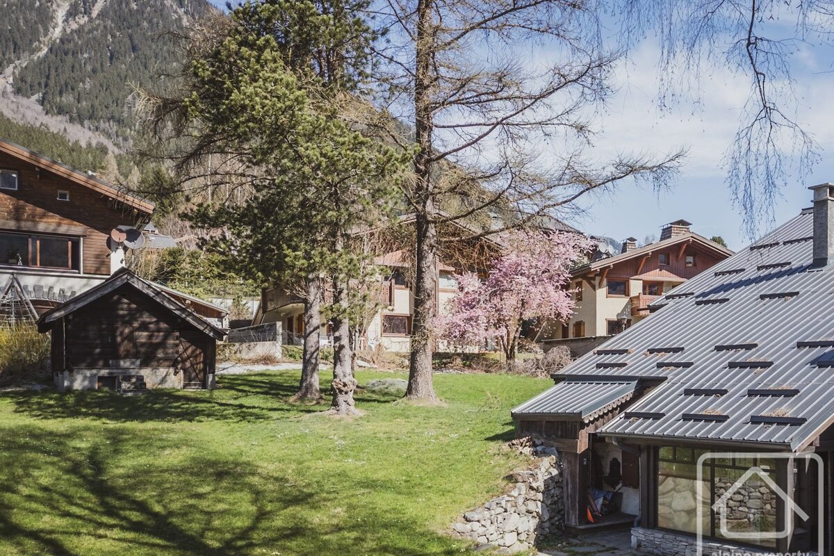 An alpine landscape featuring wooden chalets, green lawns, and tall trees under a bright blue sky.
