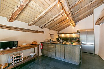 Rustic kitchen featuring exposed wooden ceiling beams, a dark wood island, slate floors, and stainless steel appliances.