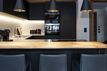Modern black kitchen featuring a light wood island countertop, bar stools, and black cone pendant lights.