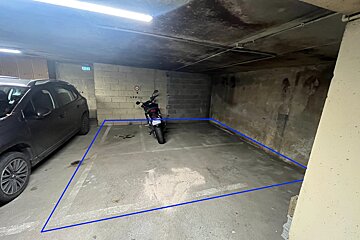 An underground parking space, outlined in blue, containing a car and a motorcycle, with concrete walls and ceiling.