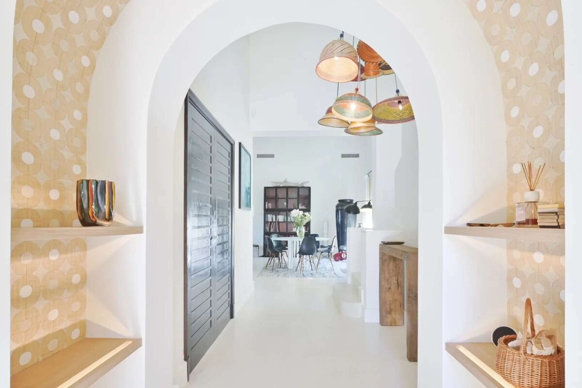 Bright arched hallway with patterned recesses, colorful woven pendant lights, and built-in shelves leading to a bright dining area.