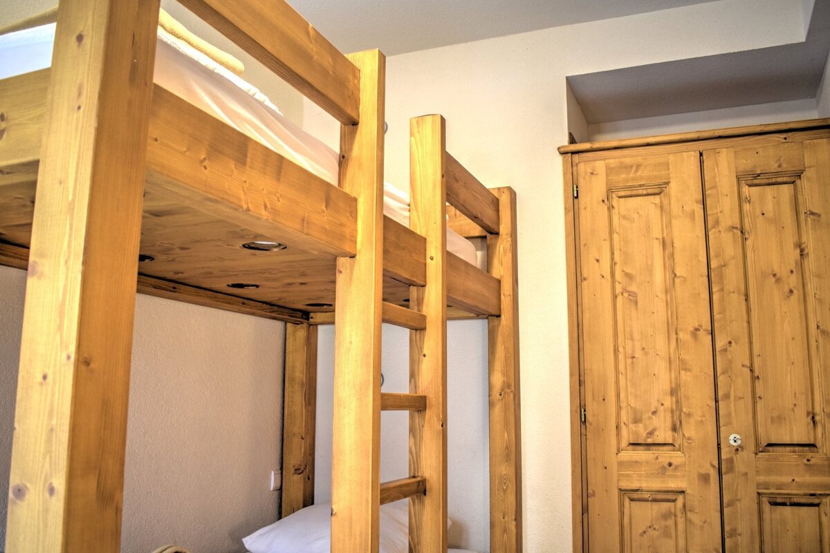 A cozy room features sturdy wooden bunk beds with built-in lights under the top bunk, alongside a matching rustic wooden wardrobe.