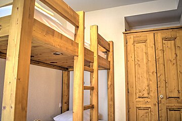 A cozy room features sturdy wooden bunk beds with built-in lights under the top bunk, alongside a matching rustic wooden wardrobe.