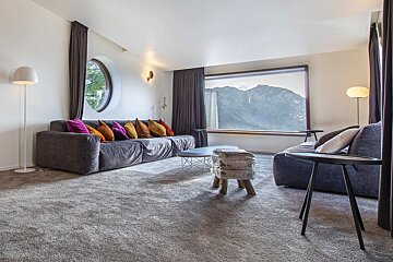 Modern living room featuring plush sofas with colorful pillows and a large window framing a scenic mountain view.