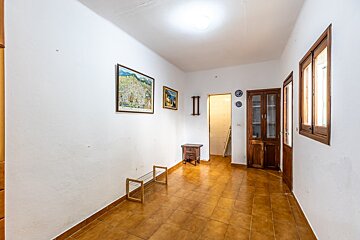 White-walled room with brown tiled floor, featuring wall art, a shoe rack, a small table, a wooden cabinet, a window, and an open doorway.