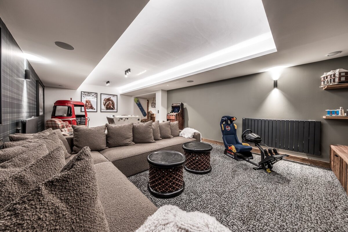 A modern, cozy entertainment room with a large sectional, racing simulator, arcade, foosball, and quirky decor like a red truck.