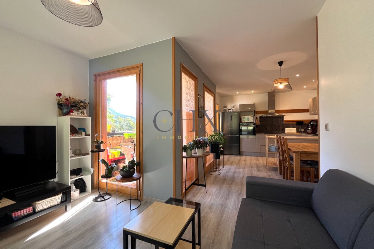 An open-plan apartment featuring a cozy living area in the foreground and a kitchen with wooden dining set in the background.