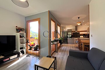 An open-plan apartment featuring a cozy living area in the foreground and a kitchen with wooden dining set in the background.