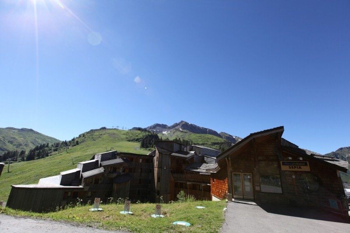 Panoramic view of a snowy mountain village nestled in a valley, surrounded by snow-capped peaks and forests with ski slopes under a clear blue sky.