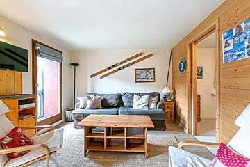 A ski-themed living room with a gray sofa, wooden coffee table, and vintage skis on the wall. It features wood paneling and a balcony door.