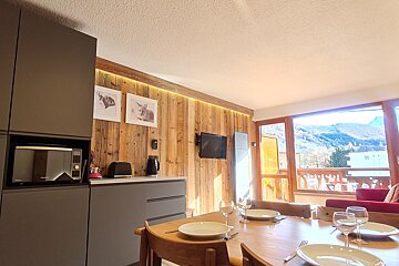 A modern kitchen/dining area with a wooden accent wall, set dining table, and a microwave. Large windows offer a scenic mountain view.
