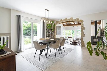 Bright, modern dining room with a dark table, plush chairs, and a rustic stone archway leading to a living area.