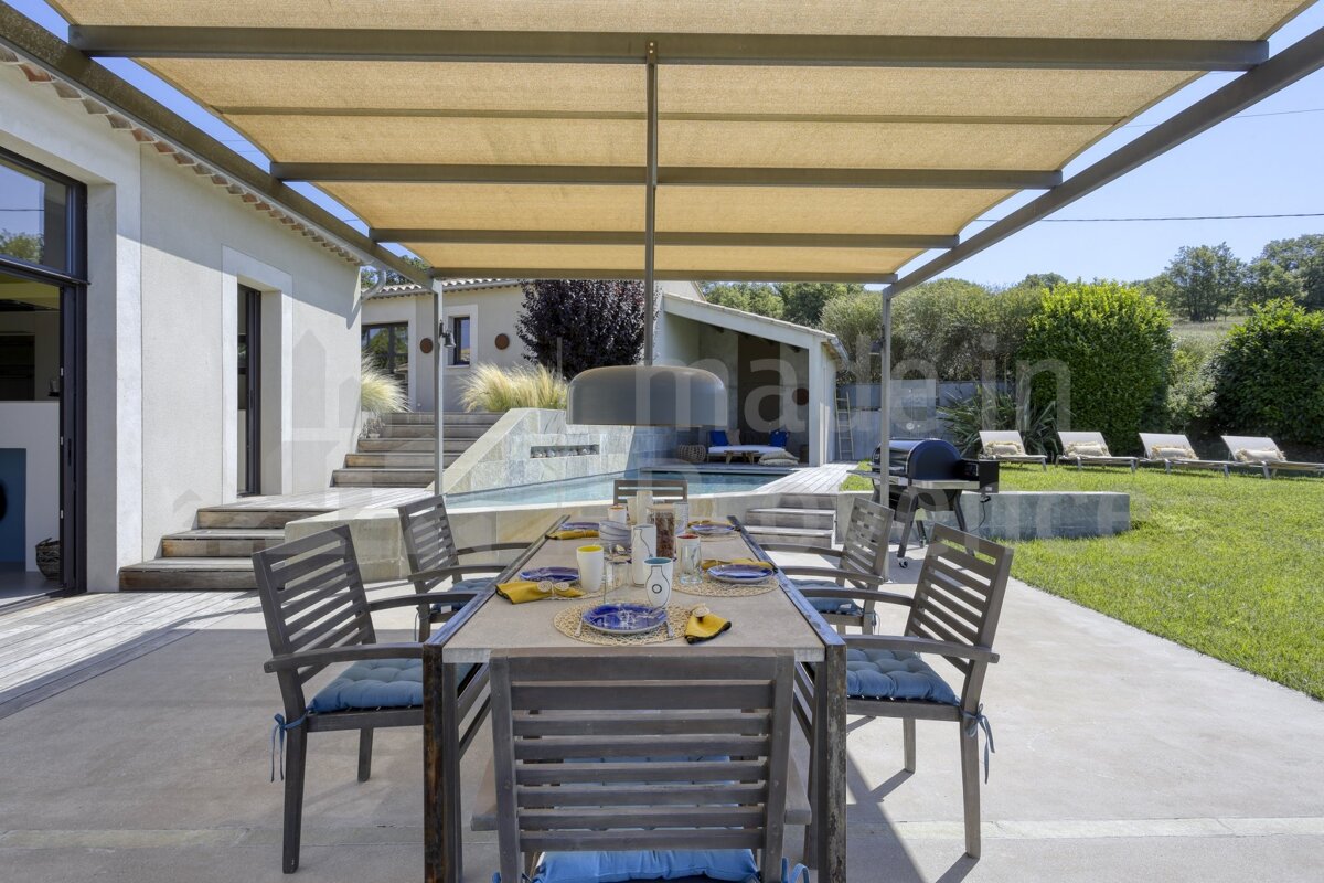 A patio with a table and chairs under a canopy with the word maison in the background