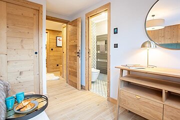 Modern chalet hallway featuring light wood doors, a bathroom entrance, and a wooden console table with a lamp and mirror.
