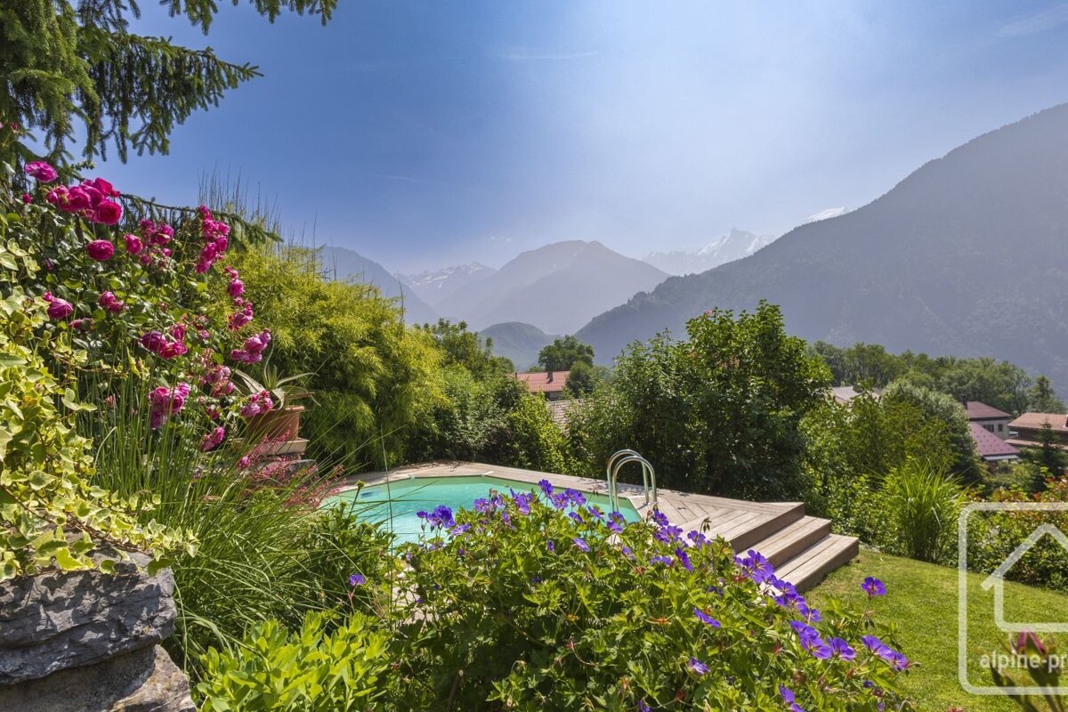 A vibrant garden with a pool, pink roses, and purple flowers overlooks majestic, misty mountains under a clear blue sky.