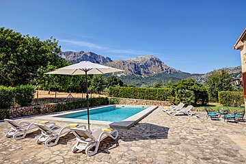 A swimming pool surrounded by chairs and umbrellas with mountains in the background
