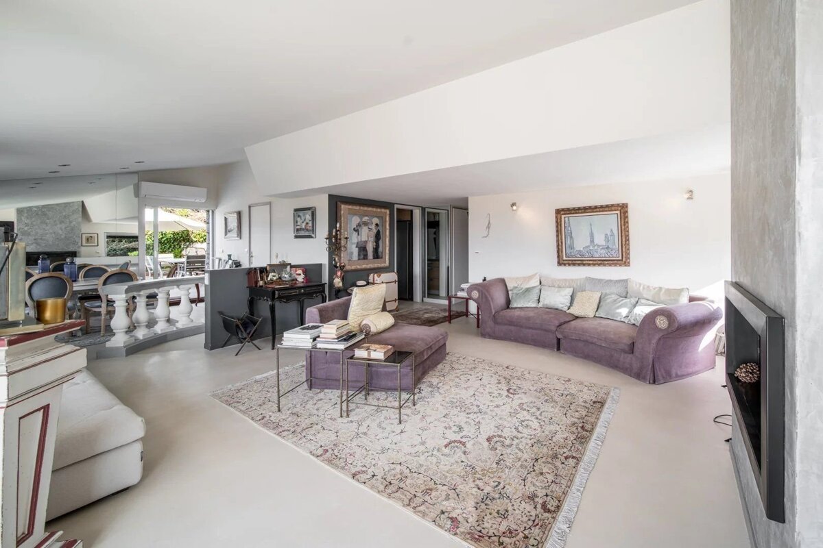 A spacious, light-filled living room featuring purple sofas, a patterned rug, and a modern open-concept layout.