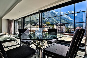 A dining room with a glass table and chairs and a view of mountains
