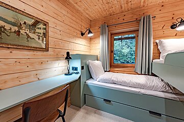 Cozy wood-paneled cabin bedroom featuring pale green bunk beds, a built-in desk with a chair, and a window with curtains.