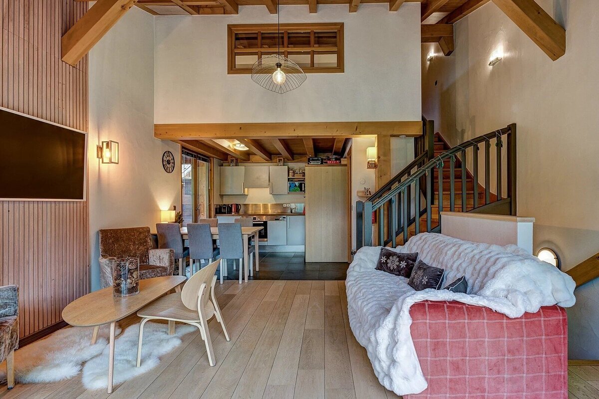 Cozy rustic-modern chalet living room with exposed wooden beams, a fluffy sofa, and a staircase leading to a loft.