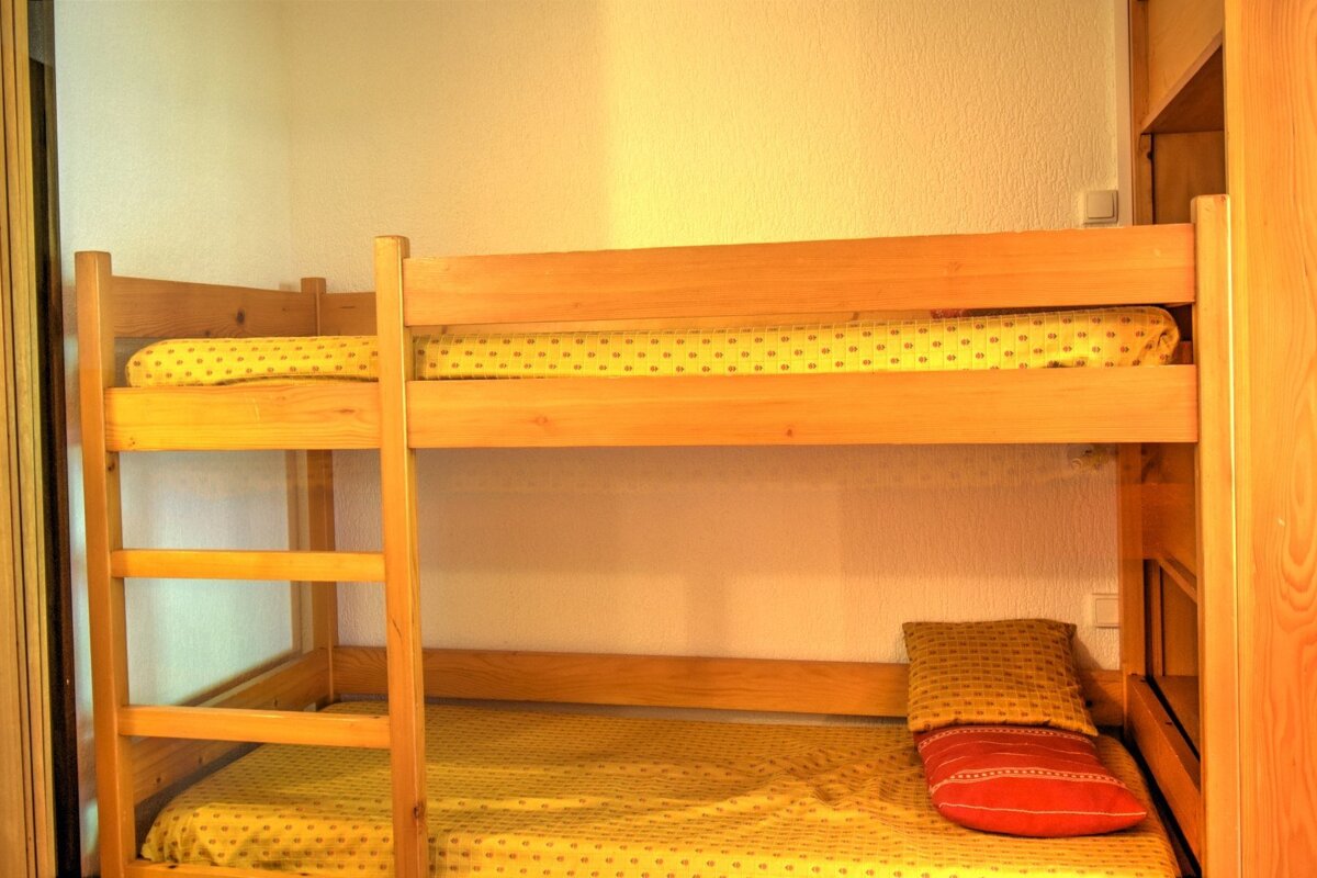 A wooden bunk bed with yellow patterned bedding and a ladder on the left. A red pillow rests on the bottom bunk.