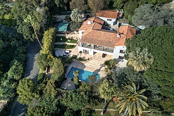 Aerial view of a luxury villa with a terracotta roof, swimming pool, and lush green gardens with palm trees.