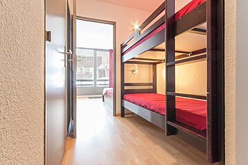 A bunk bed with red sheets in a hallway