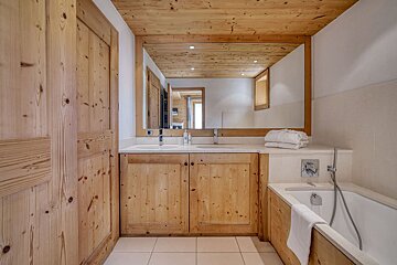 A rustic bathroom features light knotty wood walls, ceiling, double vanity with a large mirror, and a built-in bathtub.