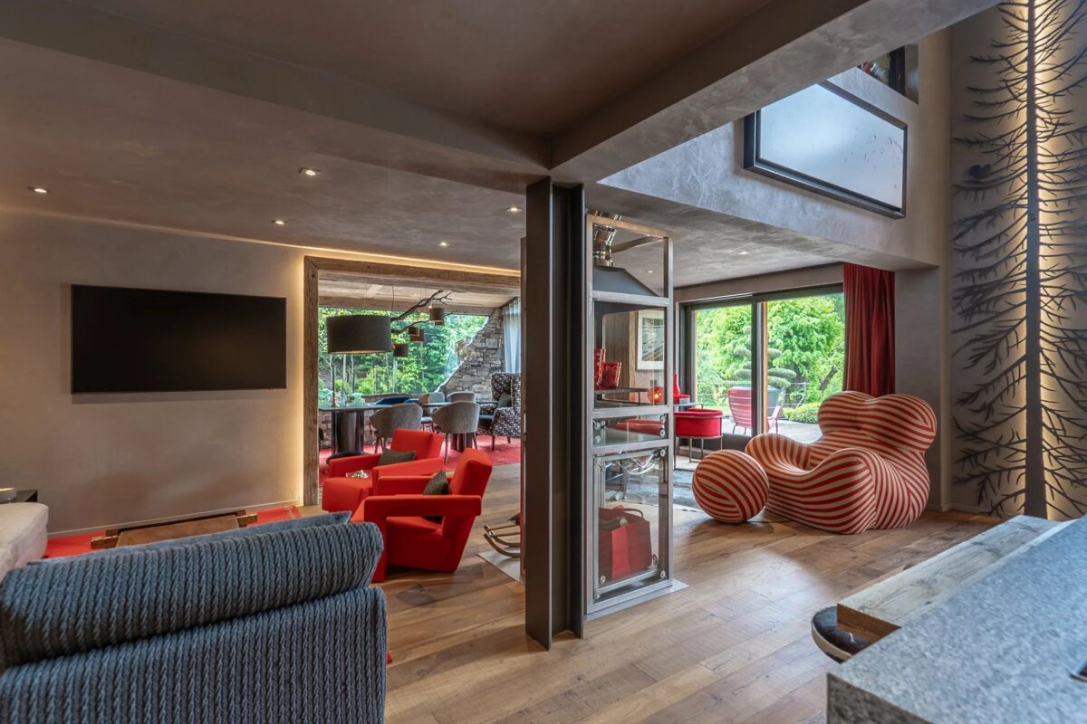 Modern, stylish living room with wooden floors, concrete walls, red armchairs, and a distinctive red-and-white striped lounge chair.