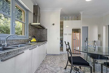 A bright, modern kitchen with white cabinets, granite counters, a window view, a striped retro fridge, and a glass dining table on a marble floor.