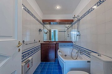 A bathroom with white tiled walls featuring blue decorative borders, blue floor tiles, a bathtub with shower, a vanity with mirror, and a toilet.