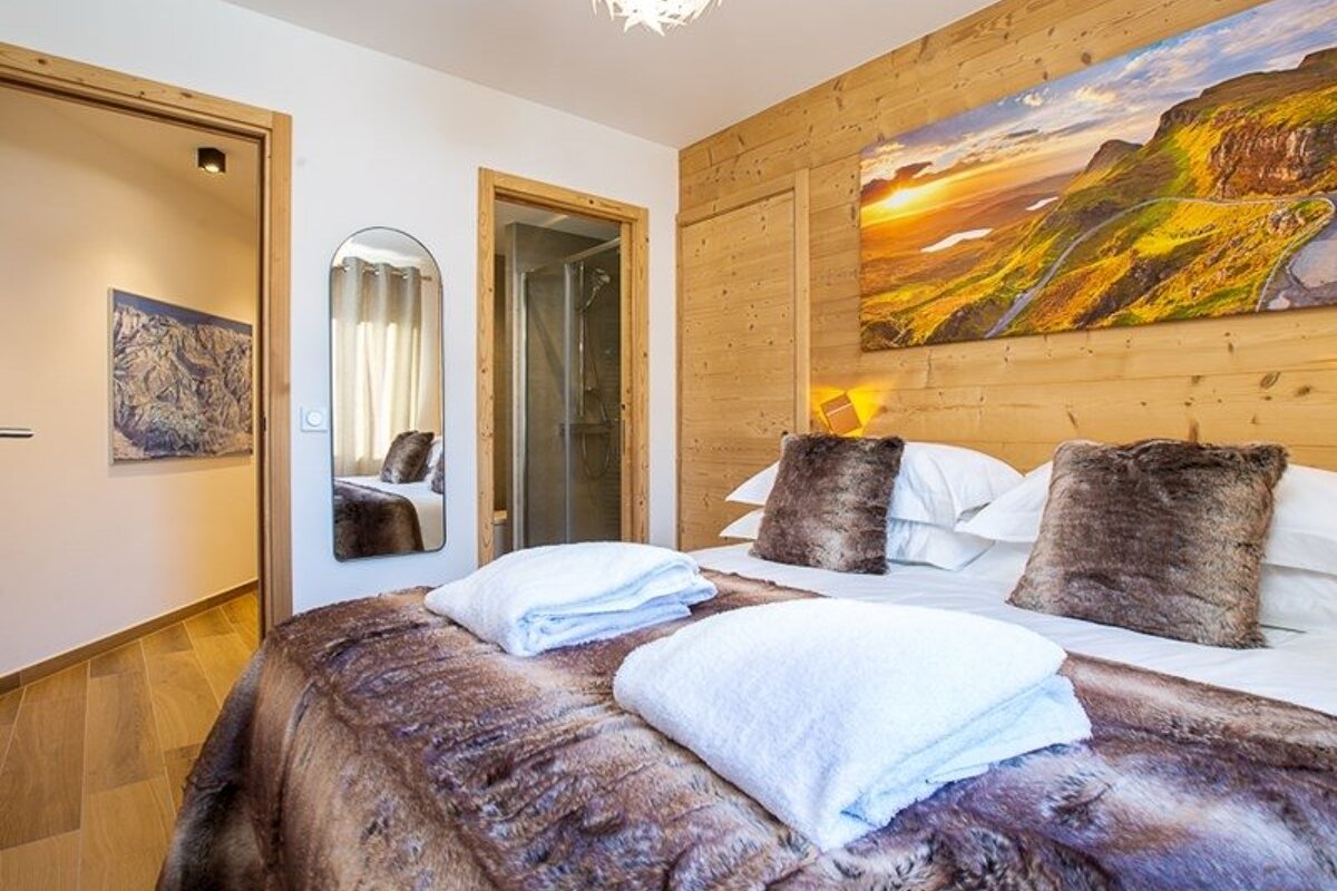Cozy alpine bedroom featuring a bed with faux-fur bedding, a wood-paneled wall with sunset art, and a doorway showing a bathroom.