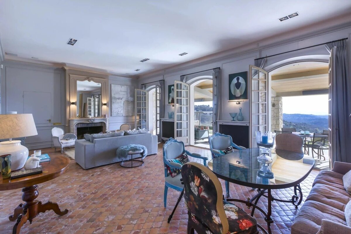 An elegant living room with terracotta tile floors, French doors opening to a scenic mountain view, and stylish, classic furniture.