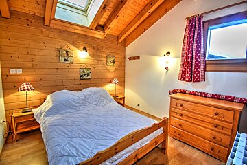 Cozy cabin bedroom with wood-paneled walls, a skylight, a bed with a white duvet, and a wooden dresser.