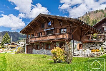 A large wooden house sits in the middle of a lush green field