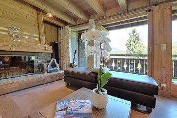 A warm chalet living room with wood paneling, a stone fireplace, large window showcasing a mountain view, and a white orchid centerpiece.