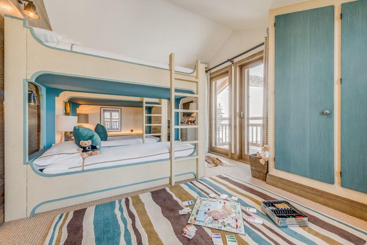 A cozy room with cream and teal custom bunk beds, a striped rug with a board game, and French doors opening to an outdoor view.