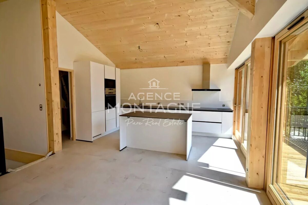A modern kitchen with white cabinets, a central island, and a light wood ceiling. Large sliding glass doors open to the outside.