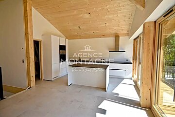 Modern kitchen with white cabinetry, a central island, and a sloped wooden ceiling. Large glass doors open to an outdoor area.