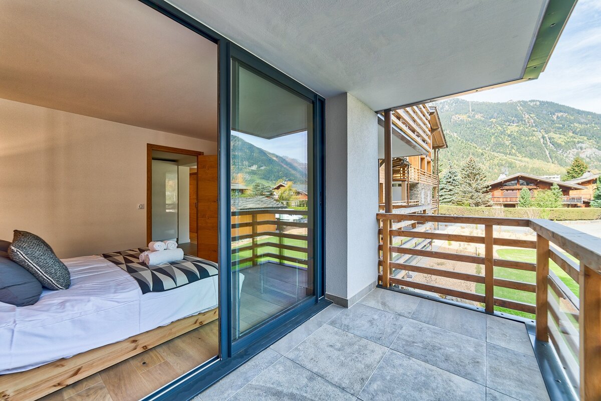 A bedroom with a bed and a balcony with mountains in the background