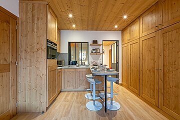 Bright, rustic-modern kitchen with light wood paneling throughout, including cabinets, ceiling, and floor. Features a small breakfast bar with stools.