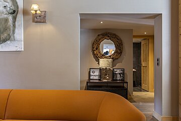 A chic living space featuring a warm orange sofa, beige walls, rustic wooden decor, and a doorway leading to another room.